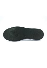 Suola in gomma nera con grip testurizzato, caratterizzata da un motivo floreale e logo "WOZ?". Lati lisci che si assottigliano verso l'alto. Design con bordo piatto e arrotondato.