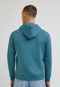 Sudadera con capucha en tejido verde azulado, con un ajuste holgado, mangas largas, puños de canalé y un bolsillo tipo canguro en la parte delantera.