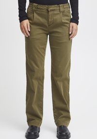 Pantalons en coton vert olive avec une coupe droite, dotés de poches avant et d'une texture lisse, associés à des bottines noires.