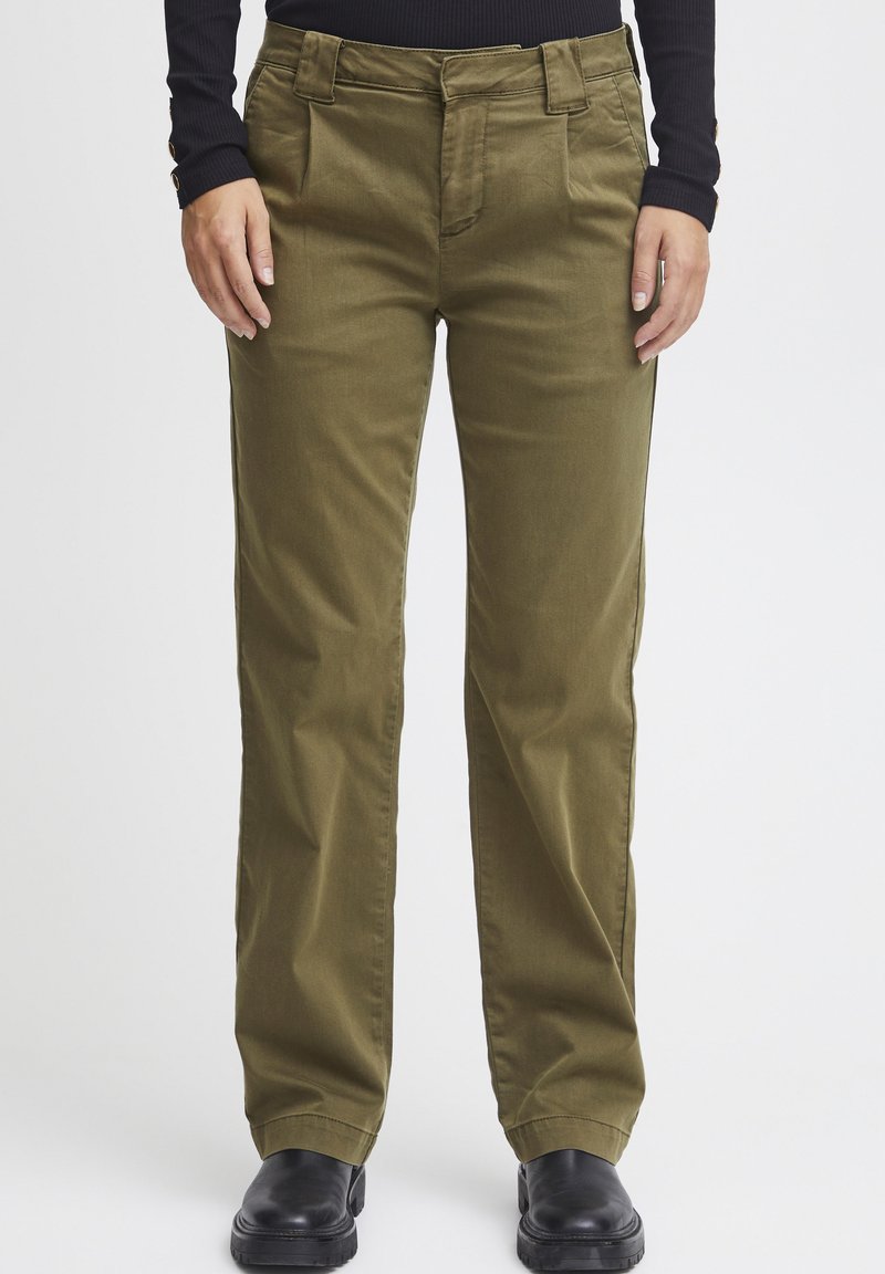 Pantalons en coton vert olive avec une coupe droite, dotés de poches avant et d'une texture lisse, associés à des bottines noires.