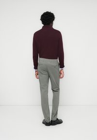 Bordeaux-coloured lange mouw turtleneck gecombineerd met lichtgrijze slim-fit broek. De broek heeft achterzakken en wordt gedragen met zwarte schoenen.