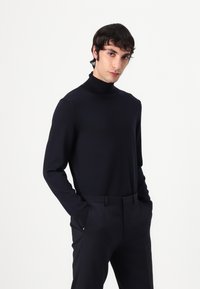 Navy turtleneck sweater made of knit fabric, featuring long sleeves and a fitted design, paired with tailored dark trousers.