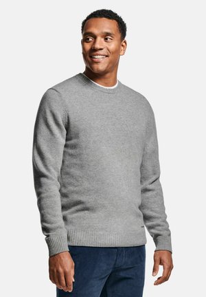 Pull en tricot gris avec un col rond et des poignets côtelés, porté par-dessus une chemise blanche, accompagné d'un pantalon bleu foncé. Texture lisse, coupe décontractée.