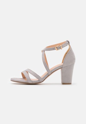 Grå ruskinds hæl-sandal med tre forreste stropper, ankelstrop med en guld spænde og en blokkheel for stabilitet.