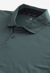 Polo-shirt vert foncé en tissu texturé, avec un col, deux boutons et une encolure intérieure en maille. Étiquette de marque visible à l'intérieur.