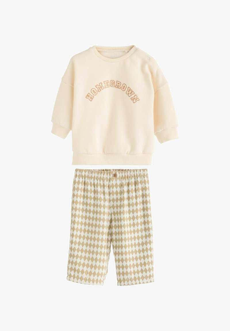 Kreemikleidiga särk, millel on helepruun "HOMEGROWN" kiri, lühikesed varrukad; beežide ja valgete rombikujuliste mustritega lühikesed püksid, millel on elastne vöökoht.