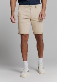Beige shorts met omgerolde zomen, gemaakt van een katoenmix. Voorzien van een knoopsluiting en zijzakken. Gemaakt met witte sokken en sneakers.