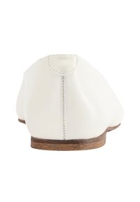 Witte leren platte schoen met een afgeronde achterkant, voorzien van zichtbare stiksels en een lage houten zool. Glad oppervlak. Eenvoudig ontwerp.