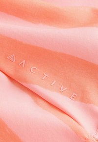 Tissu doux avec des rayures roses et corail comportant le mot « ACTIVE » et un logo triangulaire imprimé dans des couleurs assorties.
