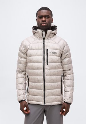 Homme portant une veste isolante Columbia Titanium gris clair avec capuche, debout devant un fond blanc uni.