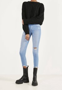 Svart kabelstickad tröja, ljusblå slitna skinny jeans och svarta chunky ankelstövlar. Anmärkningsvärda detaljer inkluderar fransad nederkant och slitna jeans.