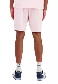 Shorts en coton rose clair avec une taille élastique, associés à des chaussettes blanches et des chaussures de sport bleues. Présentés vue de dos.