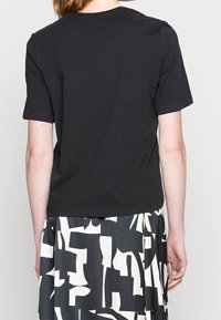 Camiseta negra de manga corta con cuello redondo. Fabricada en algodón suave, presenta un ajuste relajado y una textura lisa.