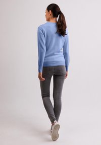 Ljusblå tröja med mjuk textur och långa ärmar, kombinerad med åtsittande grå jeans och vita sneakers. Ren, minimalistisk design.