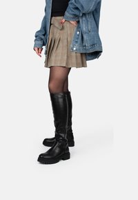 Zwarte leren laarzen tot de knie met een dikke zool, gecombineerd met een geruite geplooide rok en een spijkerjack, wat een gelaagde stijl laat zien.