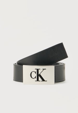 Cintura in pelle nera arrotolata con fibbia argentata che presenta un grande logo "cK" inciso.