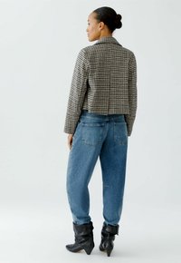Gepunktete, taillierte Jacke in Schwarz und Creme, kombiniert mit lockeren blauen Denim-Jeans. Schwarze Ankle-Boots mit spitzem Zeh und umgeschlagenem Detail.