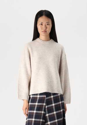 Lys beige strikket sweater med rund halsudskæring og løstsiddende pasform. Har ribbede manchetter og kant, parret med en ternet nederdel.
