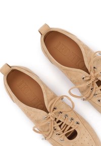 Chaussures à lacets en daim beige avec oeillets métalliques, détails perforés et semelles intérieures en cuir marron de marque, vues de dessus.