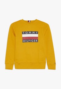 Sudadera amarilla de tejido suave que presenta un logo central con "TOMMY" y "HILFIGER" en negro y blanco, con franjas horizontales rojas y blancas.