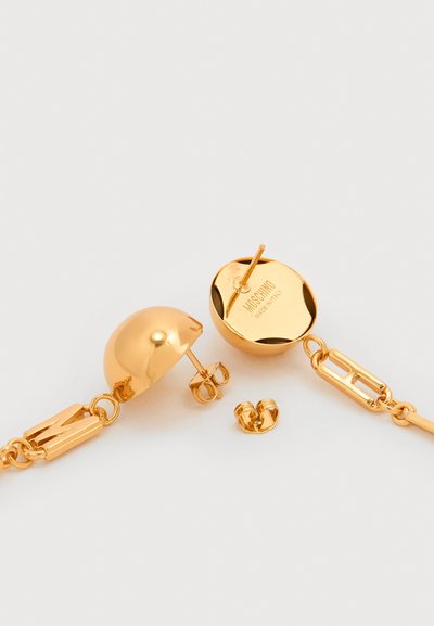 Cercei Moschino cu tija, aurii, cu design semicircular, zale de lanț și închizători de tip fluture, pe fundal alb.