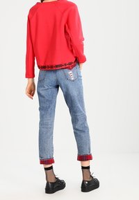 Rode sweatshirt met zwarte tekst aan de onderrand, gecombineerd met lichtblauwe jeans met een geruit manchet. Draag het met zwarte plateau-schoenen en visnetkousen.