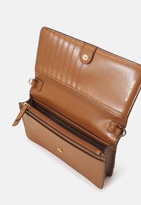 Brązowy skórzany portfel otwarty, pokazujący sześć miejsc na karty, zapinaną kieszonkę na monety, zapięcie na zatrzask oraz złote logo Michael Kors na wewnętrznej klapie.