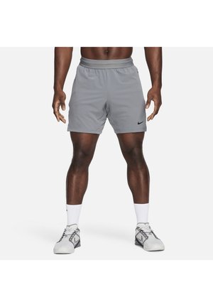 Homme portant un short de sport gris avec un logo Nike noir, des chaussettes blanches et des baskets Nike grises, debout sur fond blanc.