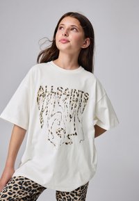 Witte oversized t-shirt met luipaardpatroon logo op de voorkant, korte mouwen en een ronde hals. Gecombineerd met luipaardprint legging.