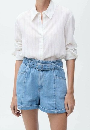 Hvid langærmet skjorte med knapper og subtile striber, indstukket i lyseblå, højtaljede denimshorts med bælte og opkrogede kanter.