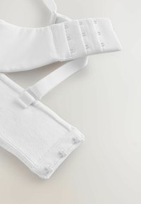 Reggiseno bianco regolabile con fascia sottostante testurizzata, spalline lisce, chiusura con gancio e asola e tessuto morbido. Design funzionale per il comfort.