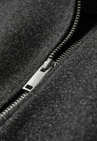 Tessuto di lana nero con vista ravvicinata di una cerniera argento. La superficie testurizzata mette in evidenza le fibre fini e i dettagli delle cuciture.