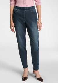 Mörk tvättade byxor med elastisk midja, slim fit och sidofickor. Framsidan har subtila sömnadsdetaljer. I kombination med mörka klackskor.