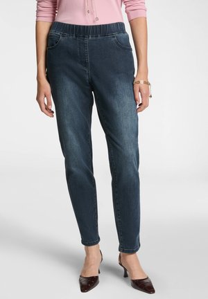 Pantaloni in denim scuro con cintura elasticizzata, dalla vestibilità slim e dotati di tasche laterali. La parte anteriore presenta dettagli di cucitura sottile. Abbinati a scarpe con tacco scuro.