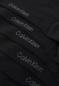 Black socks made of soft fabric, featuring the "Calvin Klein" logo in gray on the sides, stacked neatly.