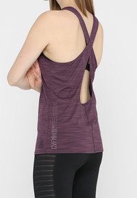Débardeur de sport violet en tissu texturé, avec un design dos nageur et un dos découpé. Associé à un legging noir à motifs rayés.