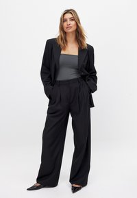 Melna pielāgota žakete virs pelēka pieguļoša topa, saskaņota ar augsto vidukli melnām platām biksēm un norādītām melnām kurpēm.