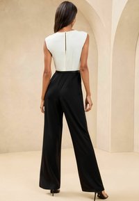 Black jumpsuit with a white, fitted bodice; features a keyhole back, wide-leg design, and thin black belt. Smooth, sleek fabric.
