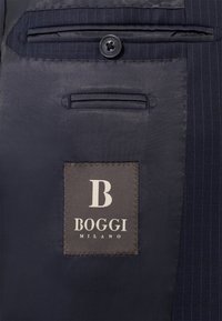 Temno modra tkanina z drobnim črtastim vzorcem, ki vsebuje črno gumb in etiketo z napisom "B BOGGI MILANO" vezanim v belem.