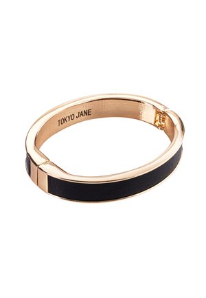 Schwarzes Lederarmband mit vergoldetem Metall, mit einer glatten Oberfläche und einem Scharnierverschluss. Im Inneren eingraviert "TOKYO JANE".