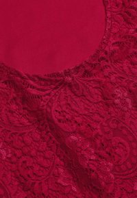 Röd spets tyg med intrikata blommönster som ligger över en slät röd bakgrund, med en scalloped kant och detaljerad broderi.