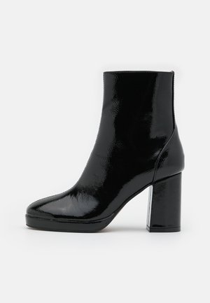 Zwarte enkellaars van lakleer met blokhak, zijrits en een licht puntige neus, afgebeeld op een witte achtergrond.