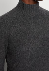 Kolgrå polotröja i mjukt stickat tyg. Har en figursydd design, ribbad krage och sömlösa axeldetaljer.