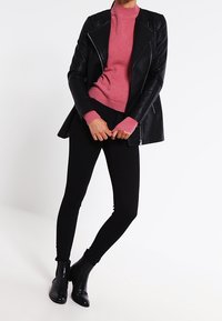 Black leather motorcycle jacket over a pink knit sweater, paired with black skinny pants and ankle boots, creating a fitted look.