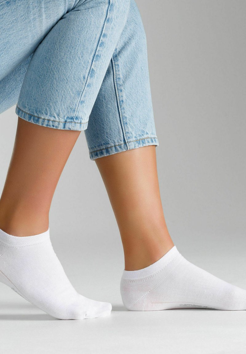 Weiße Knöchelsocken aus einem weichen, glatten Material, mit einem gerippten Bund und nahtlosem Zehendesign, getragen zu hellblauen Jeans.