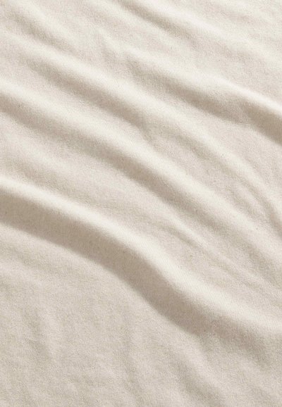 Tissu beige doux avec une fine texture et de légers plis horizontaux créant des ombres subtiles à la surface.