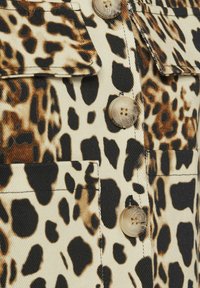 Leopardprint stof met een beige achtergrond, met grote zwarte en bruine vlekken. Knopdetails met een natuurlijke afwerking en zichtbare stiksels.