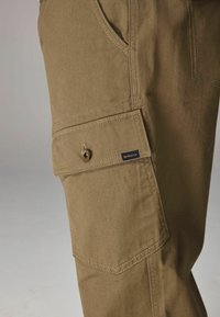 Khaki cargobroek met een zijzak met knoopsluiting, versterkte stiksels en een merklabel bij de tailleband.