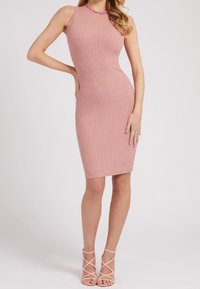 Robe en maille côtelée rose avec une silhouette ajustée, un design sans manches et un col rond. Des talons à brides couleur blush complètent le look.