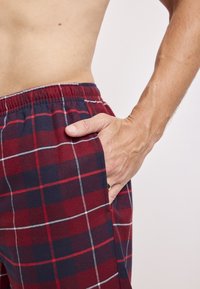 Rode en marineblauwe geruite pyjamabroek met een elastische tailleband, zijzakken en witte stiksels. Zachte stoftextuur.
